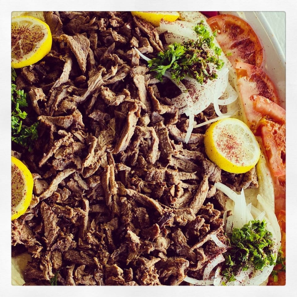 Close-up of Shish Kabob Xpress's beef shawarma with onions, tomatoes, parsley, and lemon slices.