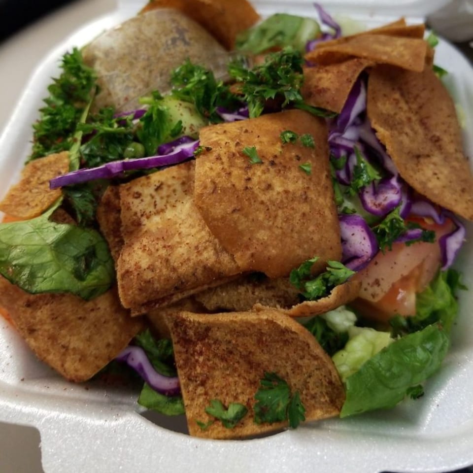 Middle-Eastern salad with lettuce, red cabbage, tomatoes, parsley, and crispy pita bread in a white container.