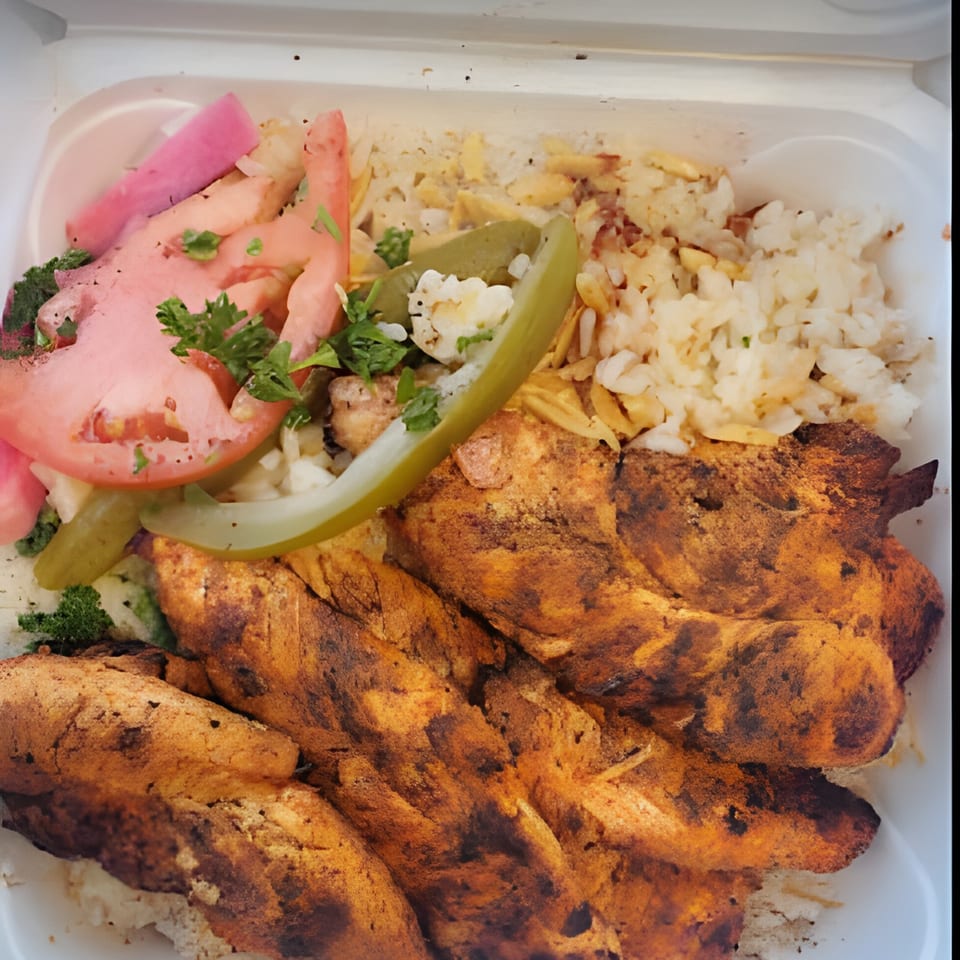 Middle-Eastern chicken and rice dish with pickled vegetables and fresh tomatoes in a white container.